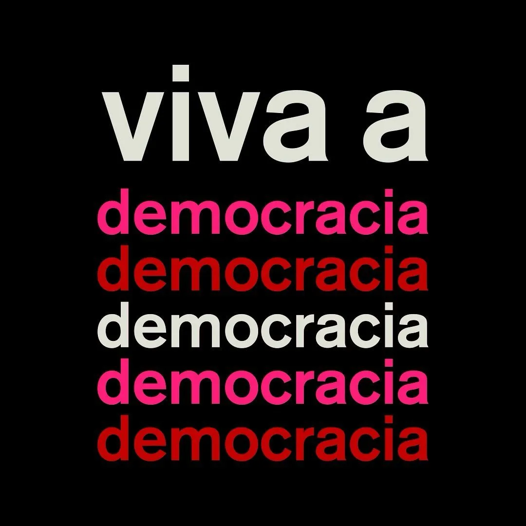 Fundo preto. “viva a” em letras claras e, abaixo, a palavra “democracia” repetida cinco vezes, alternando rosa, vermelho e branco.